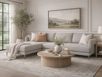 Light gray upholstered sectional with chaise, styled in an elegant living room with a round wood coffee table and wall art.