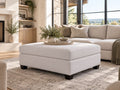 Cream upholstered ottoman in a bright, modern living room with neutral furniture and warm natural accents.