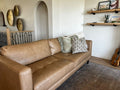 Brown leather sofa in a living room with decorative pillows and shelves in the background.