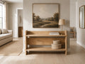 Light oak open-shelf console table styled beneath a landscape artwork in a bright modern entryway.