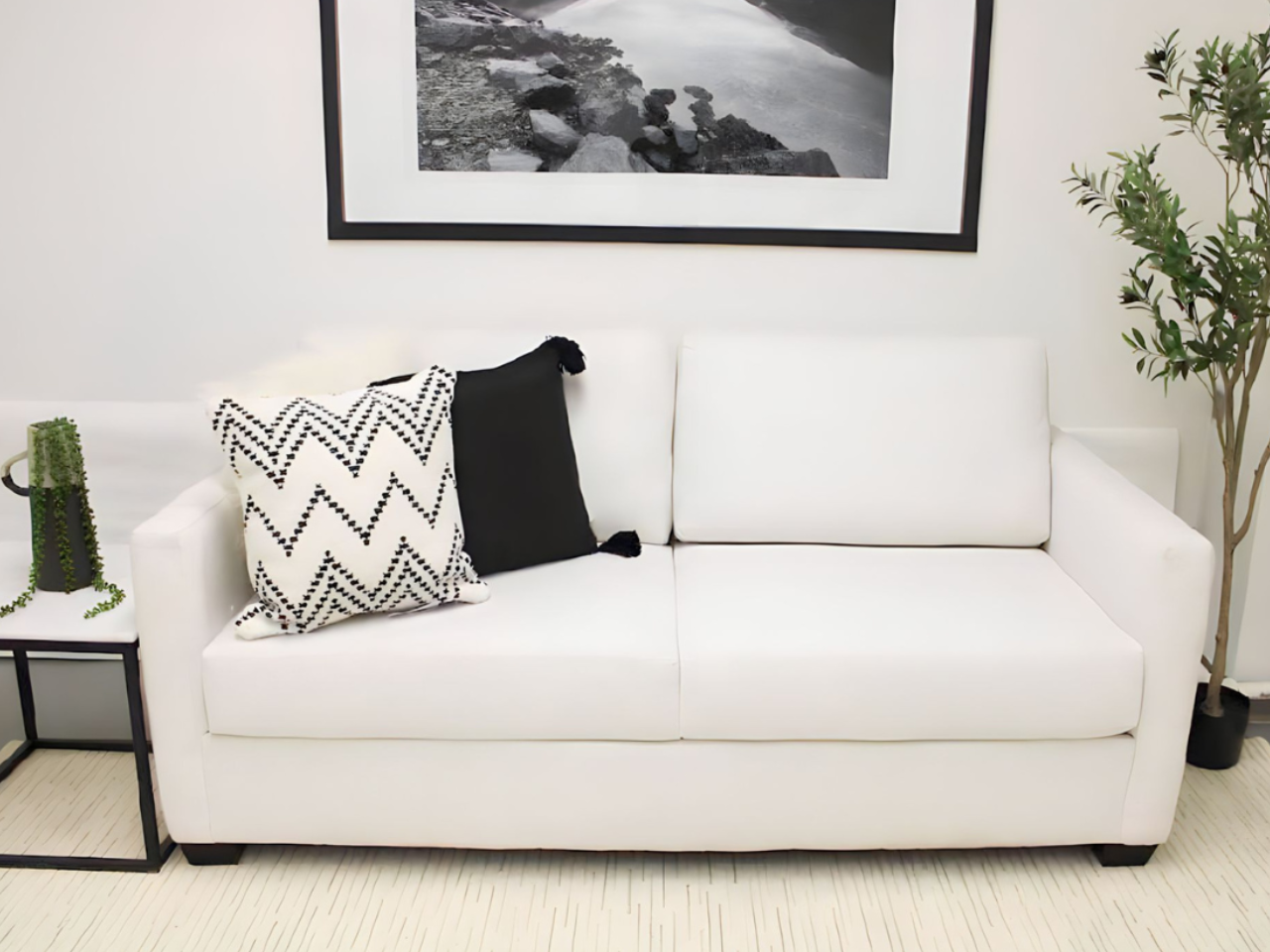 White sofabed in Calgary with decorative pillows in a room with a framed picture and plant.