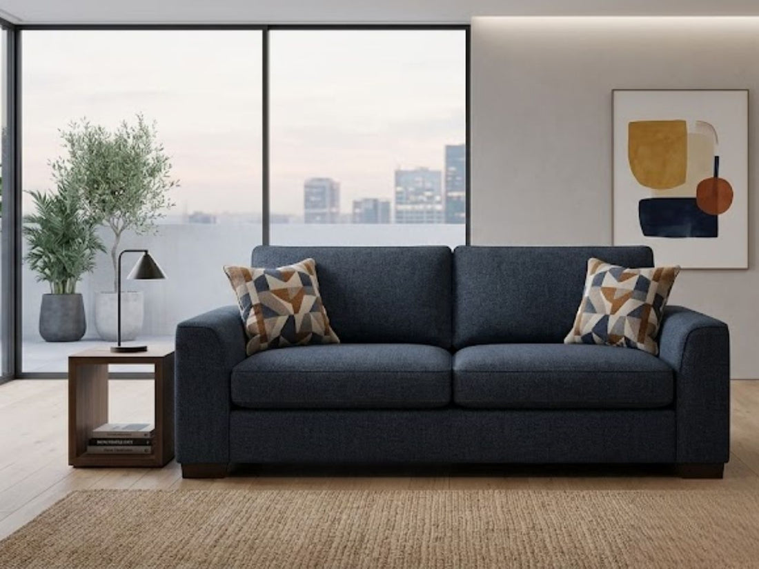Dark blue sofa in a modern living room with a side table, large windows, and abstract wall art.