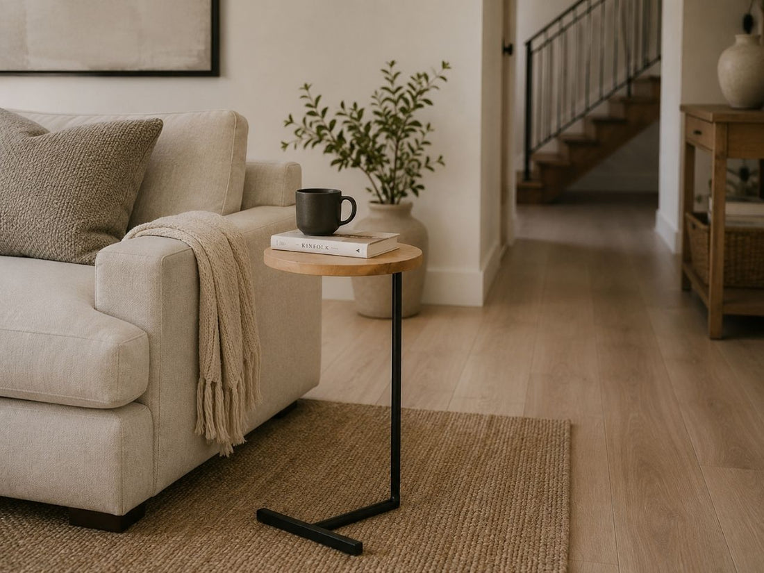 Modern C-shaped accent table with a natural wood top and black metal base styled beside a cream sofa in a cozy living room.