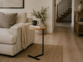 Modern C-shaped accent table with a natural wood top and black metal base styled beside a cream sofa in a cozy living room.