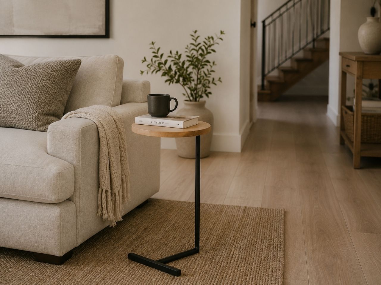 Modern C-shaped accent table with a natural wood top and black metal base styled beside a cream sofa in a cozy living room.