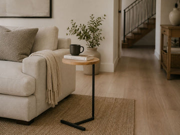 Modern C-shaped accent table with a natural wood top and black metal base styled beside a cream sofa in a cozy living room.
