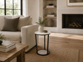 Modern round marble side table with black metal frame styled beside a cream sofa in a cozy living room.