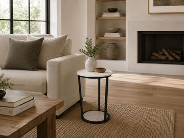 Modern round marble side table with black metal frame styled beside a cream sofa in a cozy living room.