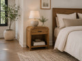 Natural wood one-drawer accent table styled as a bedside table with a ceramic lamp in a modern bedroom.