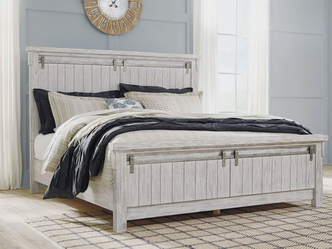 A rustic, white-washed wooden panel bed featuring a tall headboard and matching footboard with vertical planking and decorative sliding barn door hardware.