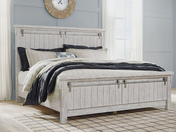 A rustic, white-washed wooden panel bed featuring a tall headboard and matching footboard with vertical planking and decorative sliding barn door hardware.