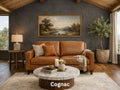 A compact two-cushion cognac leather loveseat sits against a dark charcoal-gray accent wall under a vaulted wood-plank ceiling.