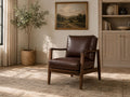 Brown leather accent chair with a wooden frame in a modern neutral living room.