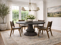 A round dark dining table with wooden chairs in a bright, modern dining room.