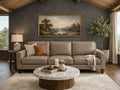 leather sofa positioned against a dark charcoal-gray accent wall under a vaulted wood-plank ceiling. A large, gold-framed landscape painting of a river hangs centered above the sofa.