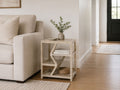 Light wood side table with geometric open shelving styled beside a cream sofa in a modern living room.