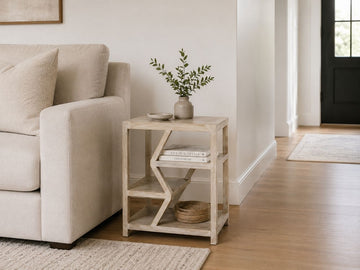 Light wood side table with geometric open shelving styled beside a cream sofa in a modern living room.