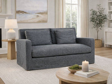 Castlerock gray upholstered loveseat styled in a bright living room with a side table and lamp.