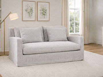 Frost gray upholstered loveseat styled in a bright living room with a floor lamp and framed wall art.