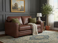 Dark brown leather loveseat with plush cushions, set in an elegant living room with neutral accents.