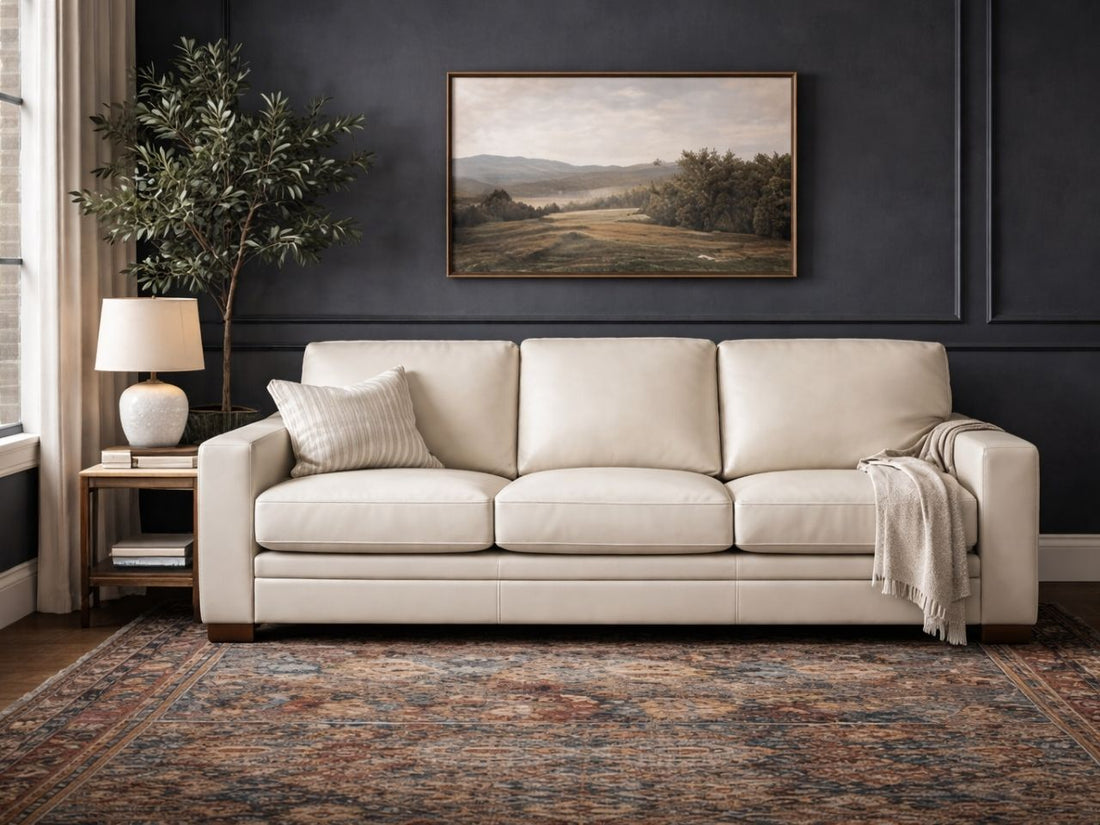 Cream three-seat sofa upholstered in smooth leather or leather-look fabric, styled in an elegant living room with dark walls.