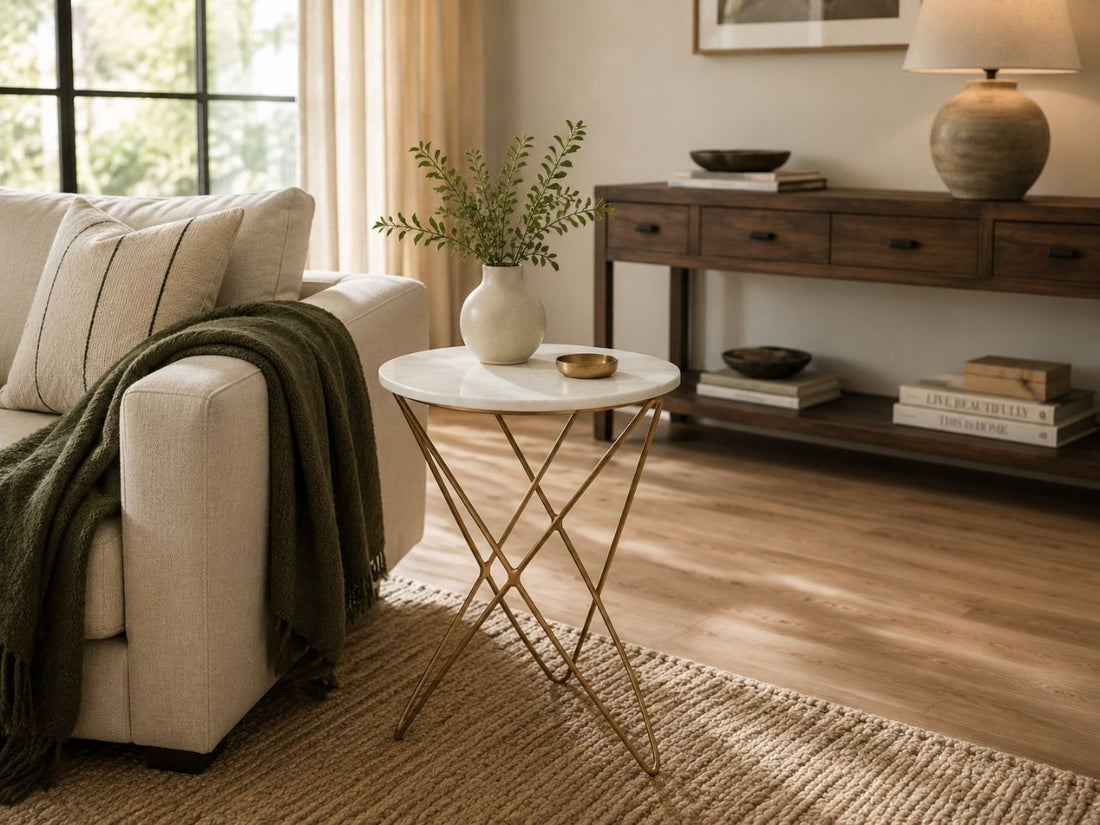 Contemporary marble-top side table with gold geometric metal base styled beside a neutral sofa in a warm living room.