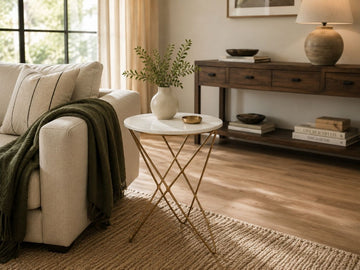 Contemporary marble-top side table with gold geometric metal base styled beside a neutral sofa in a warm living room.
