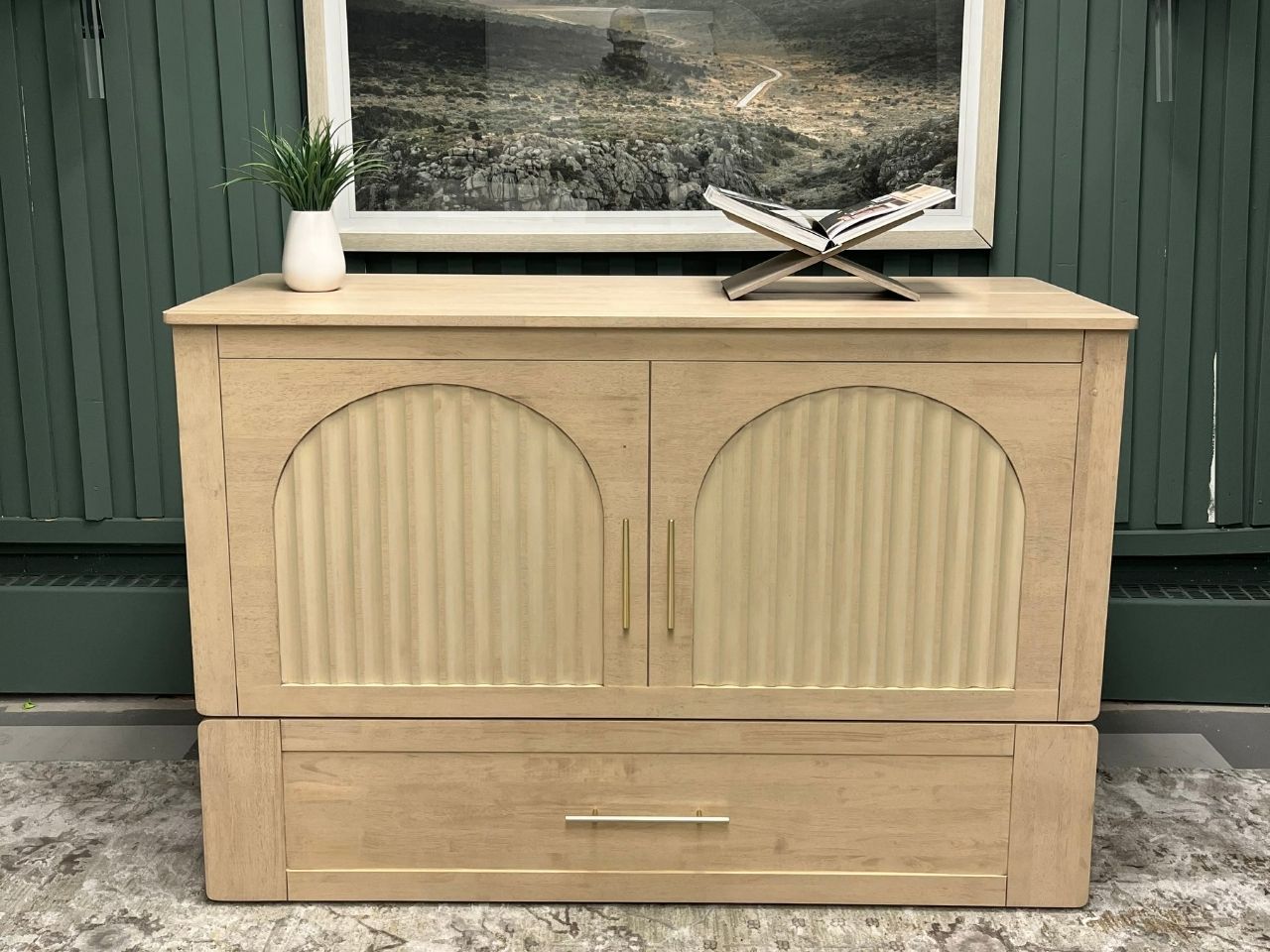 Light wood cabinet bed with arched fluted doors and brass hardware, photographed in a showroom setting.