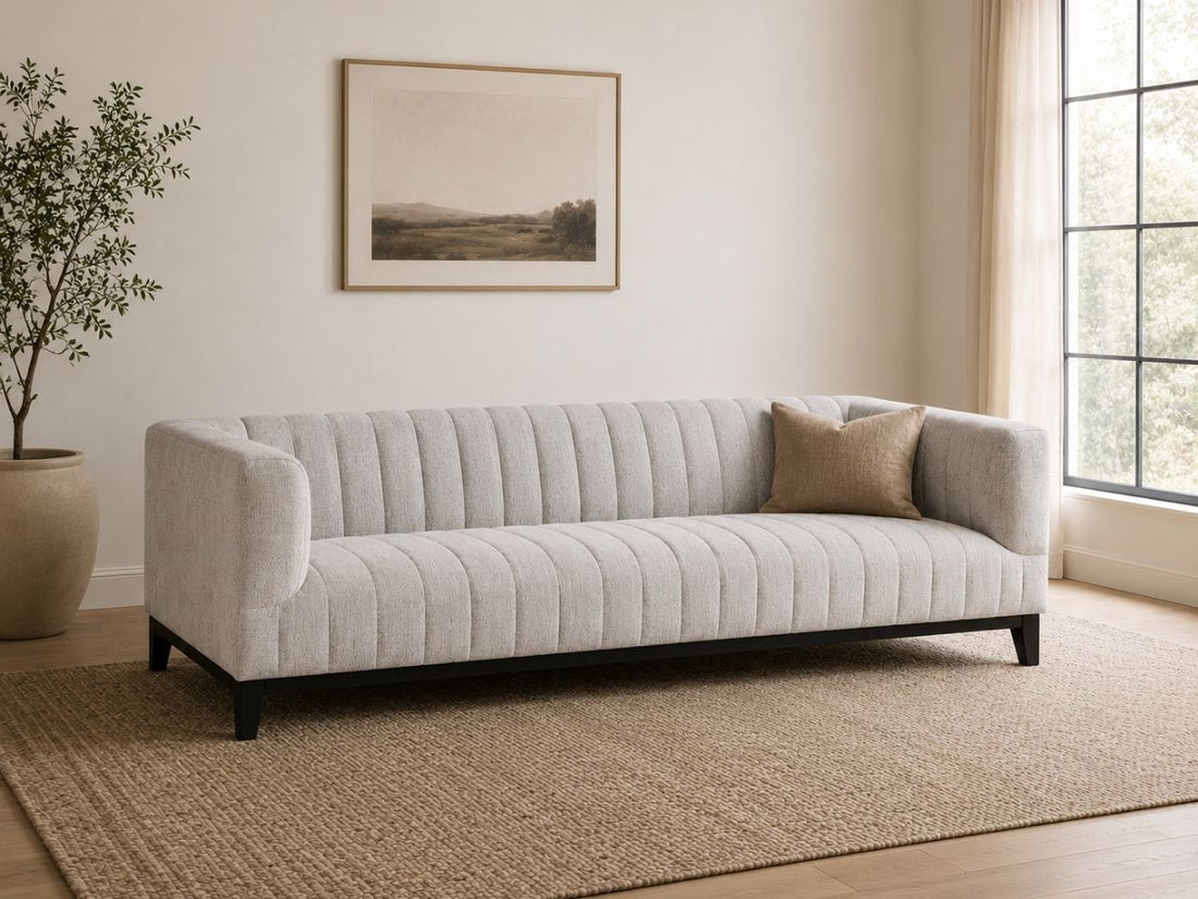 Light channel-tufted sofa with accent pillow in a modern, neutral living room.