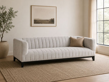 Light channel-tufted sofa with accent pillow in a modern, neutral living room.