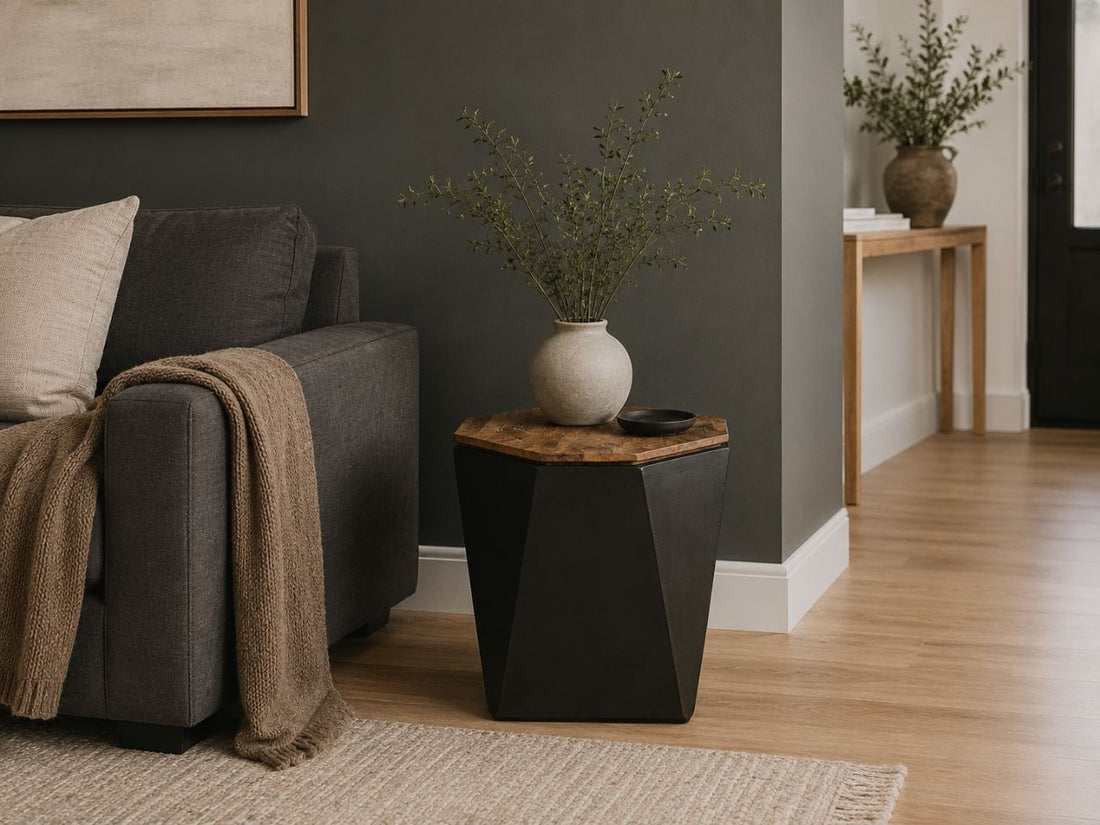 Black geometric accent table with a natural wood top styled beside a charcoal sofa in a contemporary living room.