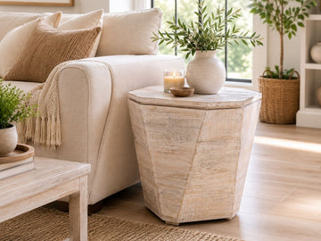 Light brown geometric wood side table with a faceted design, styled beside a cream sofa in a bright modern living room.