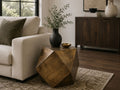 Geometric gold metal side table with a faceted design styled beside a cream sofa in a contemporary living room.