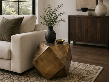 Geometric gold metal side table with a faceted design styled beside a cream sofa in a contemporary living room.