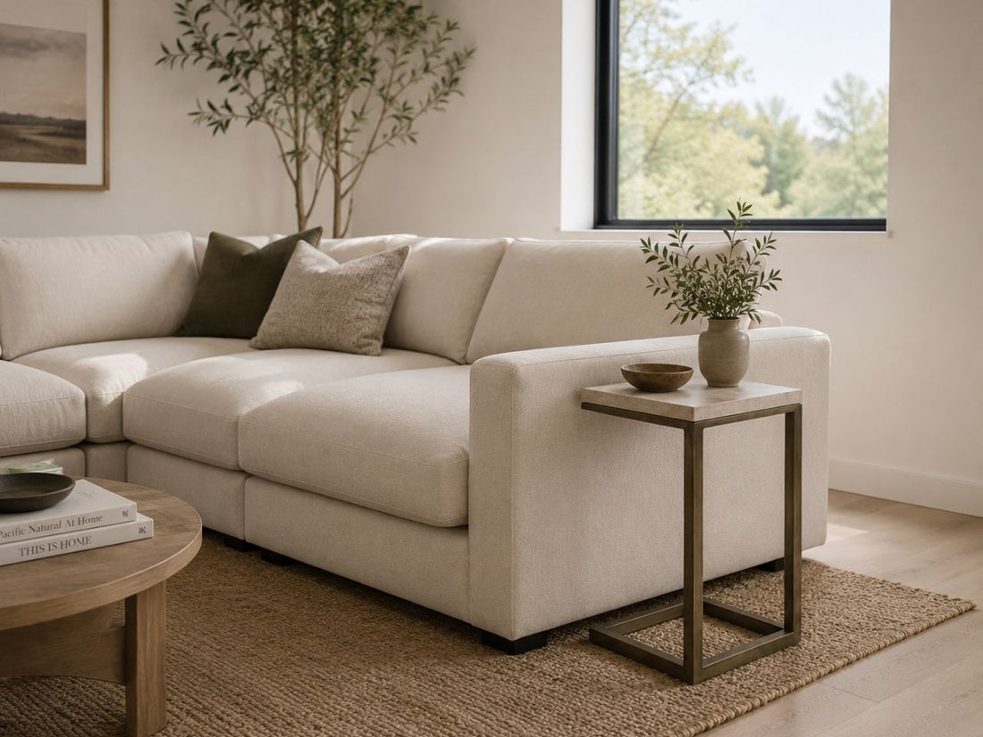 Light brown C-shaped side table with a metal frame, styled beside a cream sectional in a modern neutral living room.