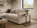Light brown C-shaped side table with a metal frame, styled beside a cream sectional in a modern neutral living room.