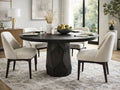 Dark wood round dining table with sculpted pedestal base and upholstered chairs in a bright dining room.