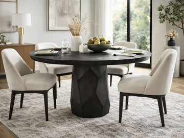 Dark wood round dining table with sculpted pedestal base and upholstered chairs in a bright dining room.