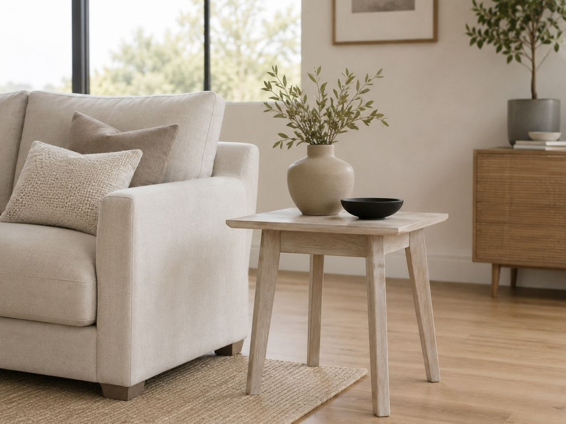 Light wood side table with a simple square top and angled legs, styled beside a cream sofa in a Scandinavian-inspired living room.