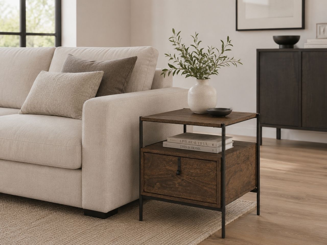 Dark wood end table with a drawer, open shelf, and black metal frame, styled beside a cream sofa in a contemporary living room.