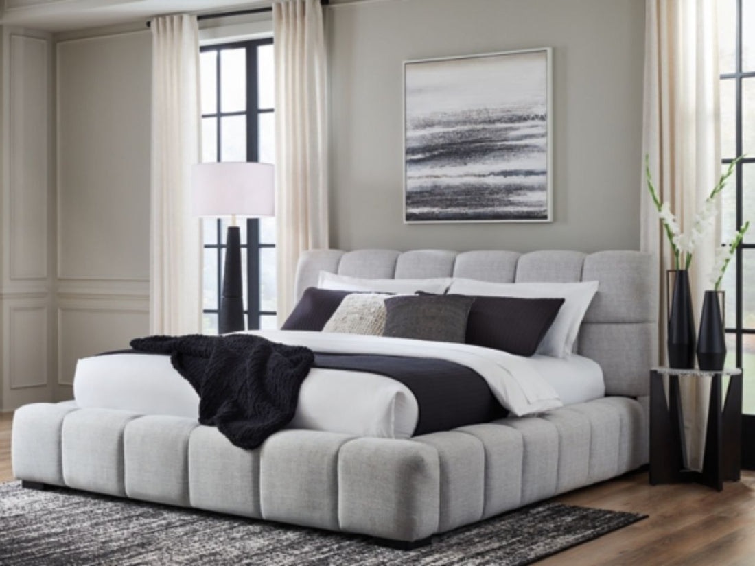 Light gray upholstered bed styled in a bright, modern bedroom.
