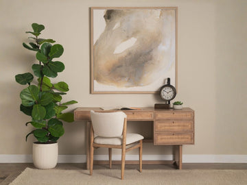 A styled home office scene featuring a light wood desk with cane-front drawers and a matching upholstered chair.