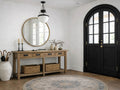 A rustic, four-drawer wooden console table with dark metal inset pulls, styled in a bright entryway featuring a white brick wall and a large black arched door. 