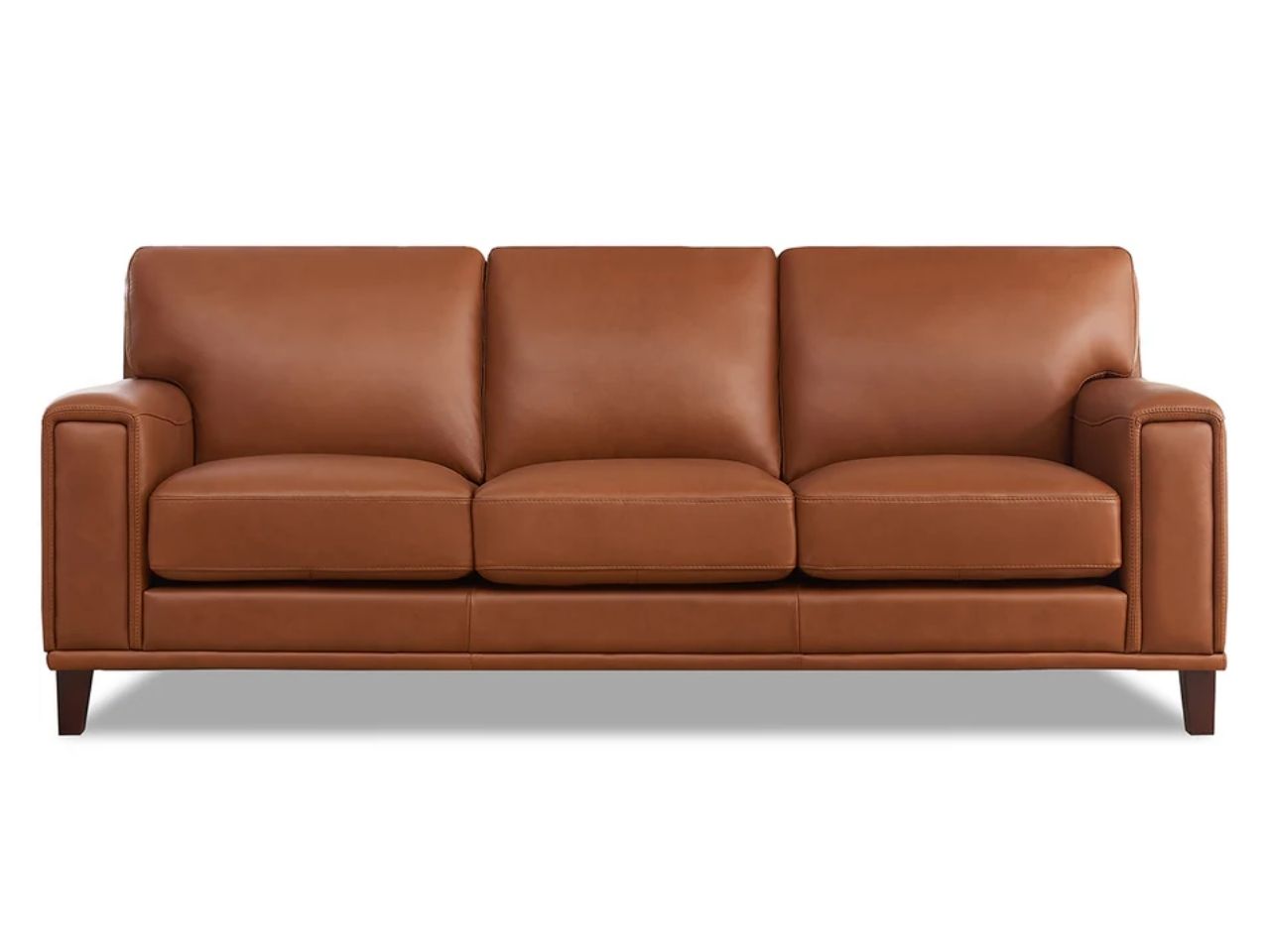 A modern three-seat leather sofa with a sleek silhouette, slim legs, and smooth seat cushions, upholstered in warm caramel brown leather and photographed on a white background.
