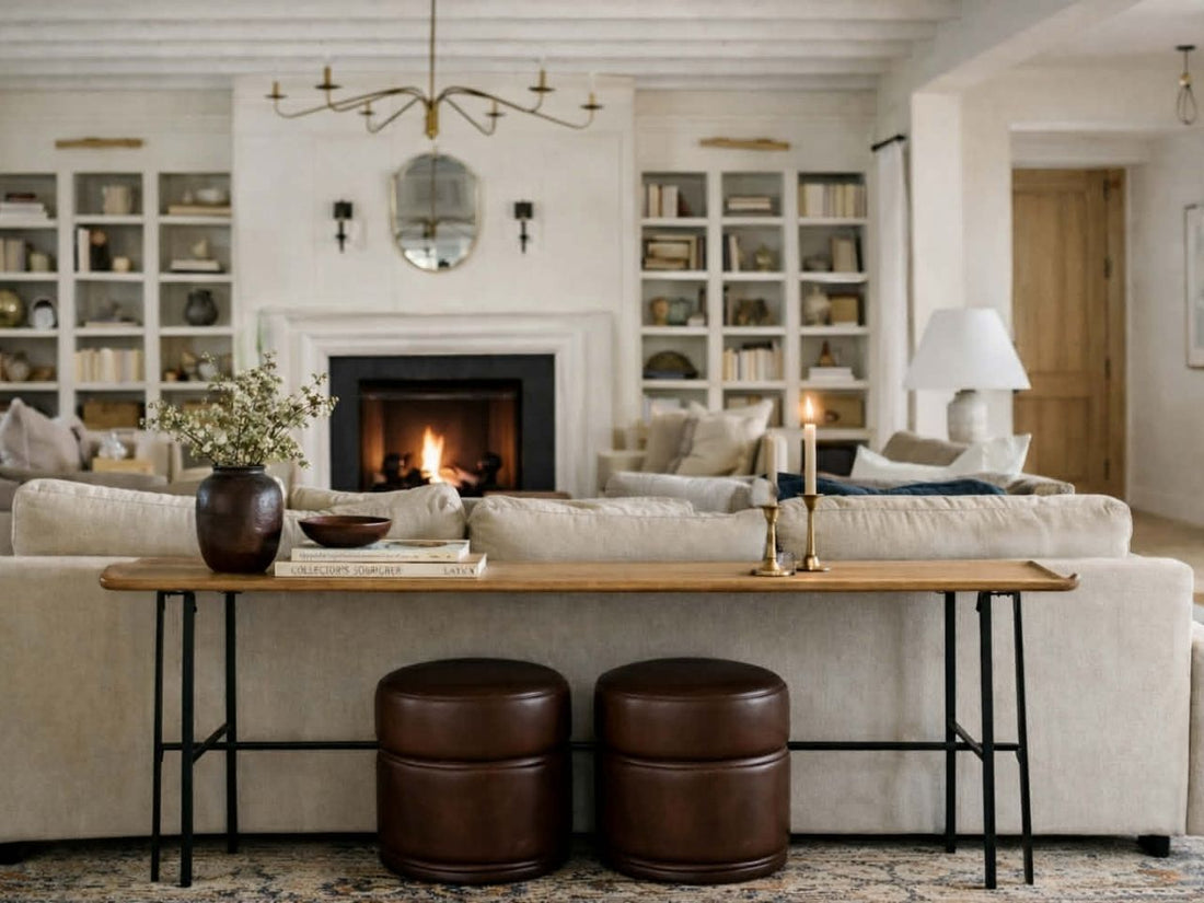 A long, slender wooden console table with thin black metal legs sits behind a beige sofa. 