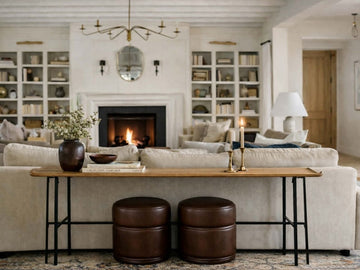 A long, slender wooden console table with thin black metal legs sits behind a beige sofa. 