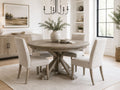 Round driftwood dining table with four upholstered dining chairs in a bright farmhouse-style dining room.