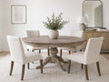 Round driftwood pedestal dining table with four cream upholstered chairs in a bright modern dining room.