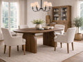 Oval wood dining table with curved pedestal legs, surrounded by cream upholstered dining chairs in a bright, airy dining space.