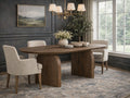 Oval wooden dining table with pedestal base, styled with neutral upholstered chairs in an elegant dining room with dark paneled walls.